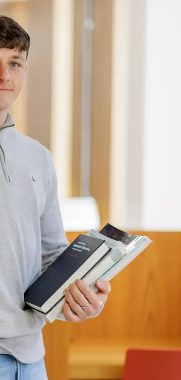 A student stands at brown shelves in the library