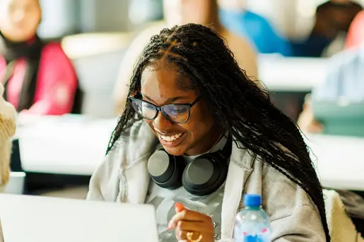 Student with headphones round neck smiling at laptop