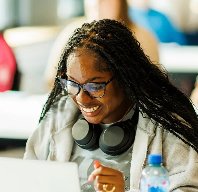 Student with headphones round neck smiling at laptop