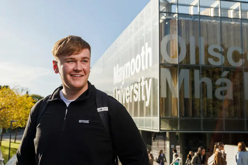 A student stands in front of our library and a brilliant blue sky