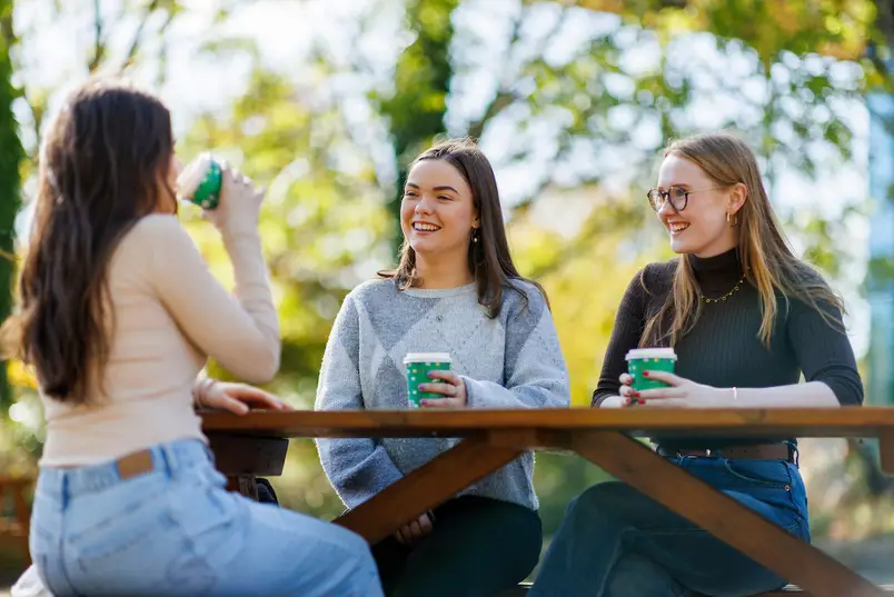 3 students sit at an outside table having coffee