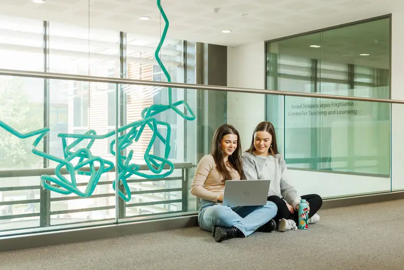 Two students sit near the Scribble statue in our Education Building