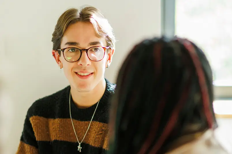 Two students talk to each other, one has their back to the camera