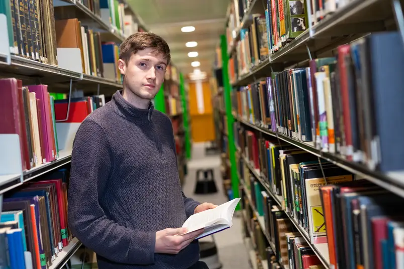 A student stands between shelves in the library