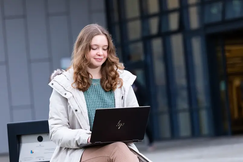 A student in a white coat sits outside Iontas